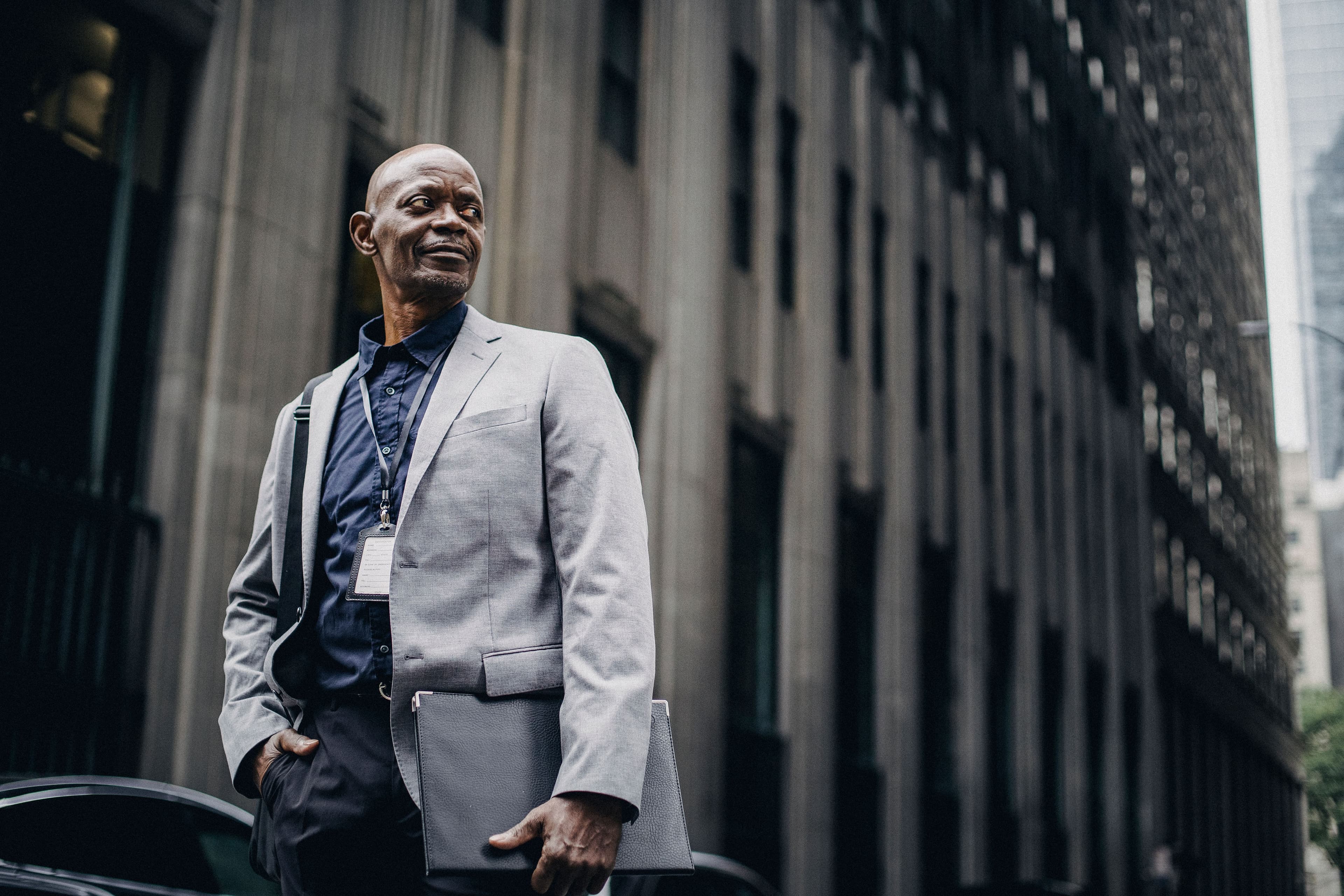 A professional wearing a lanyard and holding a portfolio outside an office building
