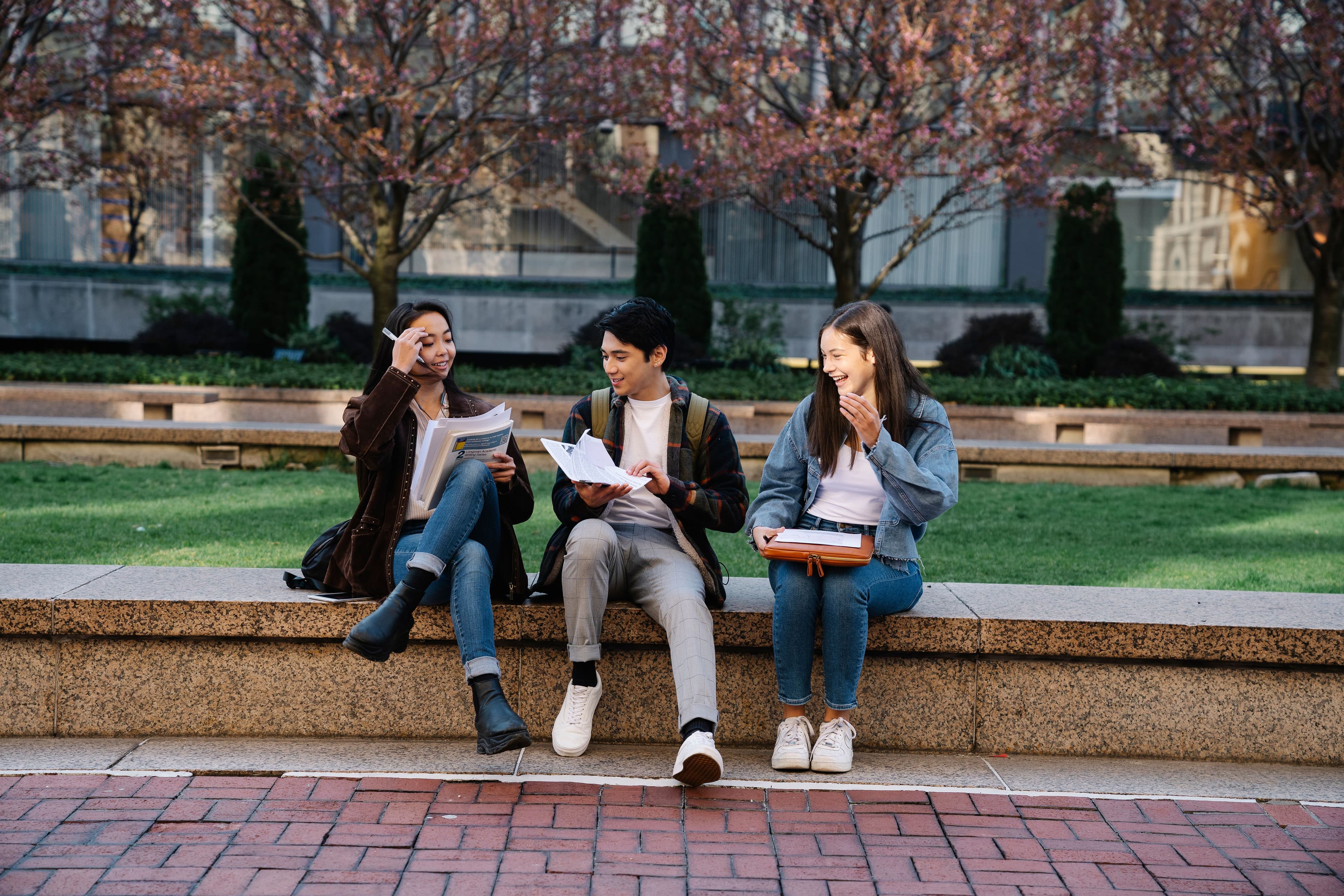 Three students sitting together on a campus bench, reviewing notes