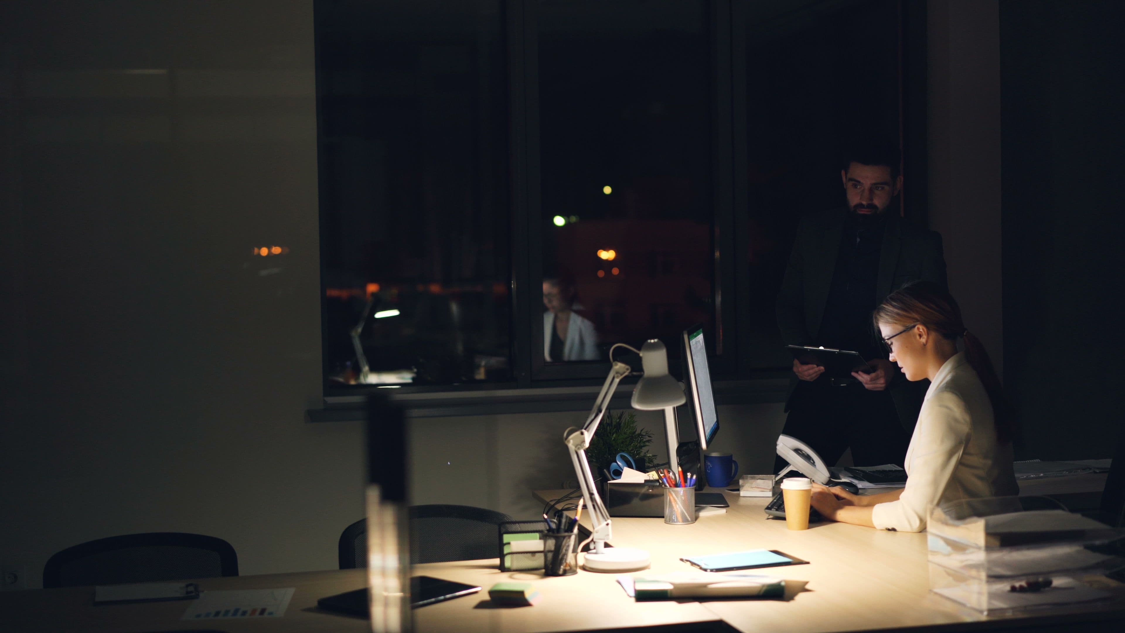 Colleagues reviewing work together at a desk in an office at night